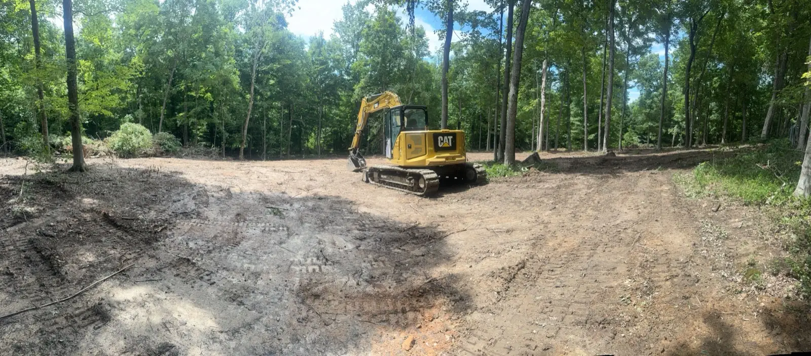 Excavator on a cleared building pad under a summer sky
