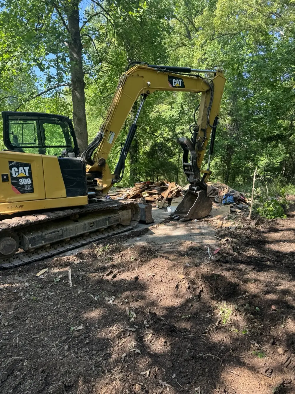 Excavator picking through debris where an old shed came down on a wooded lot
