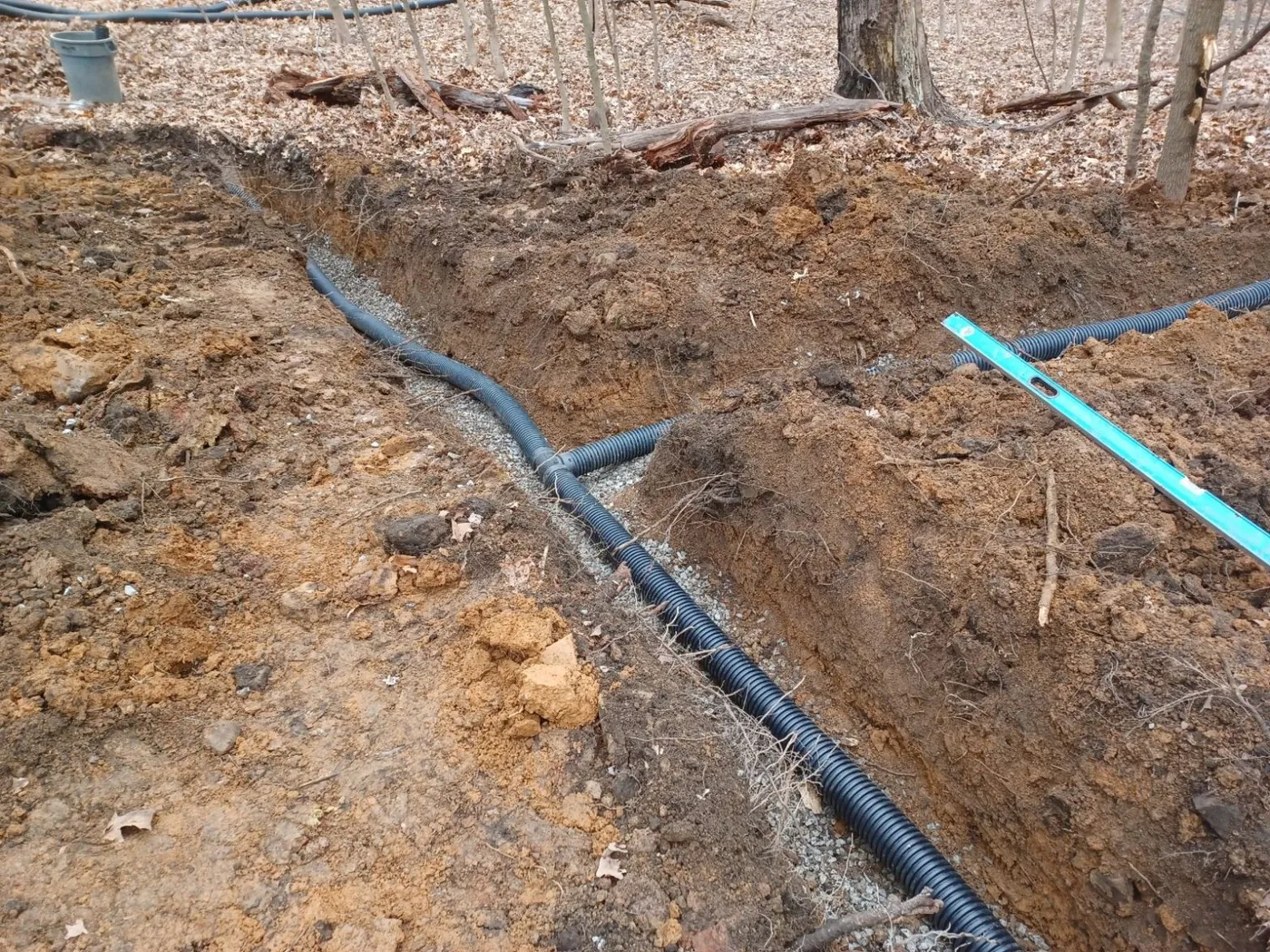 Corrugated drain pipe laid in a trench across a wooded yard