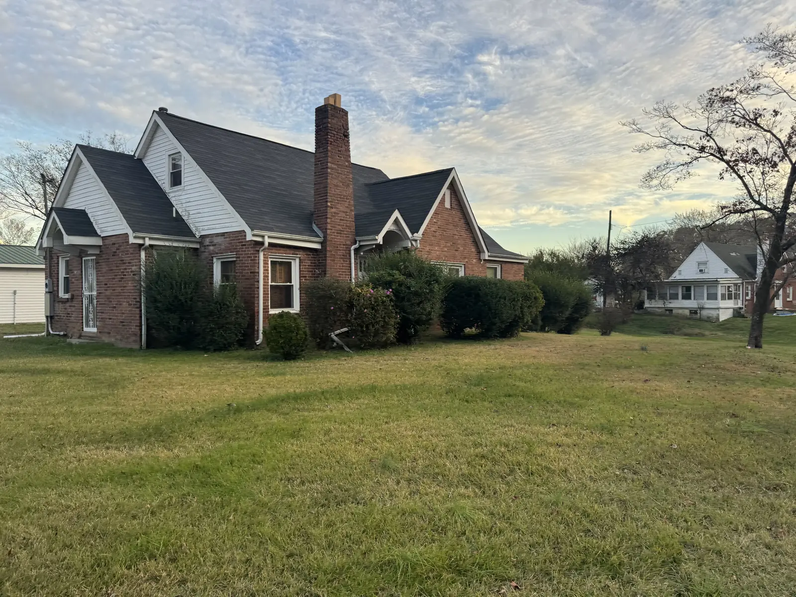 Old brick house with a chimney and hedges across the front, before demolition