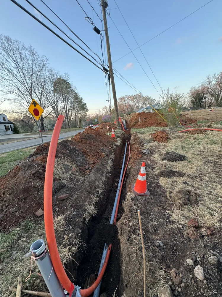 Utility trench along a roadside with orange conduit and traffic cones