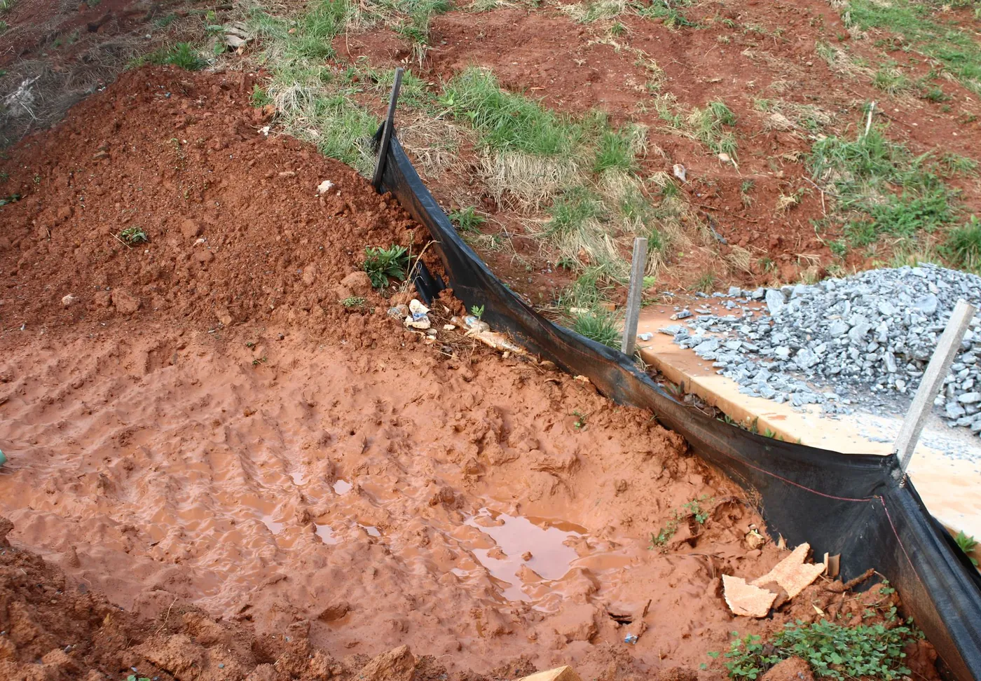 Silt fence at the bottom of a red clay slope with a stone outlet