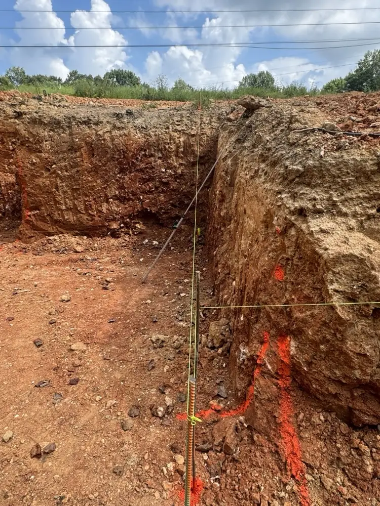 Deep trench in red clay with a grade rod set for depth