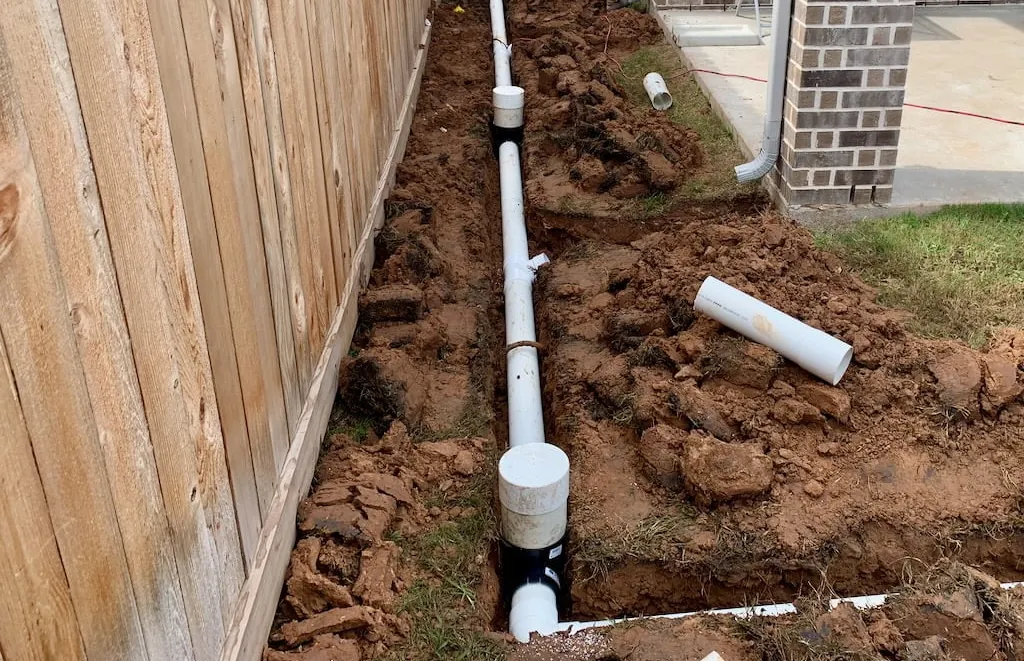 Drain line and cleanout set in a trench along a backyard fence
